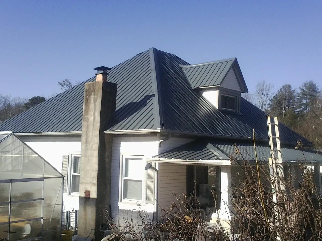 Dark blue standing seam metal roof on a white farmhouse with dormer — Slate & Tile Roof Repair by Roofing Brothers in River Falls