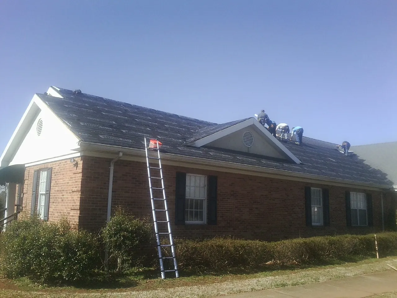 Crew tearing shingles off a brick ranch roof with a ladder set — Emergency Roof Repair work by our crew in River Falls