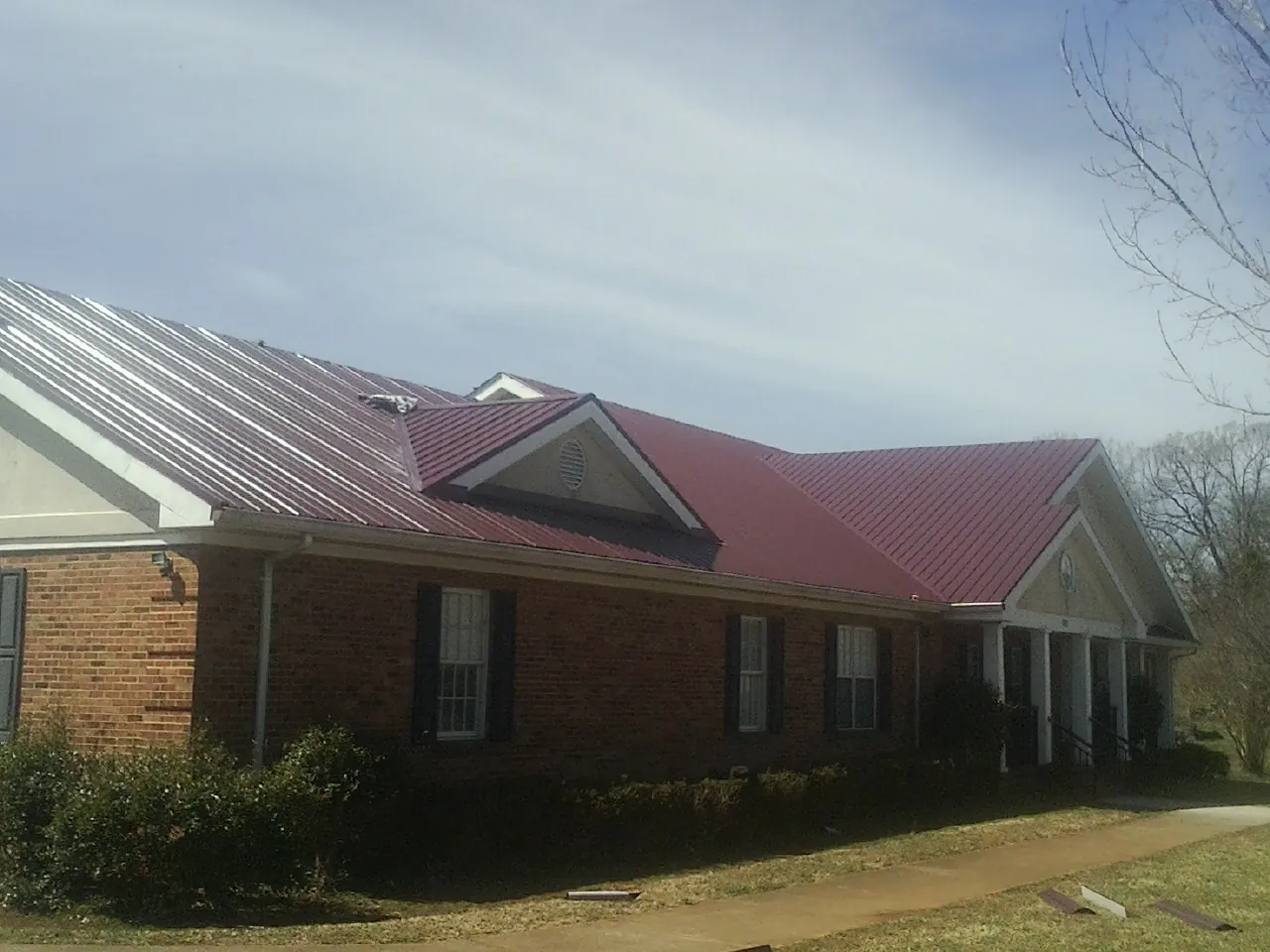 Red metal roof with gabled entries on a long brick building, from a Hail Damage Roof Repair job in River Falls