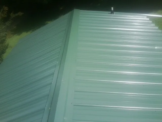New green metal panels meeting at the ridge of a roof — Flat Roof Repair work by our crew in River Falls