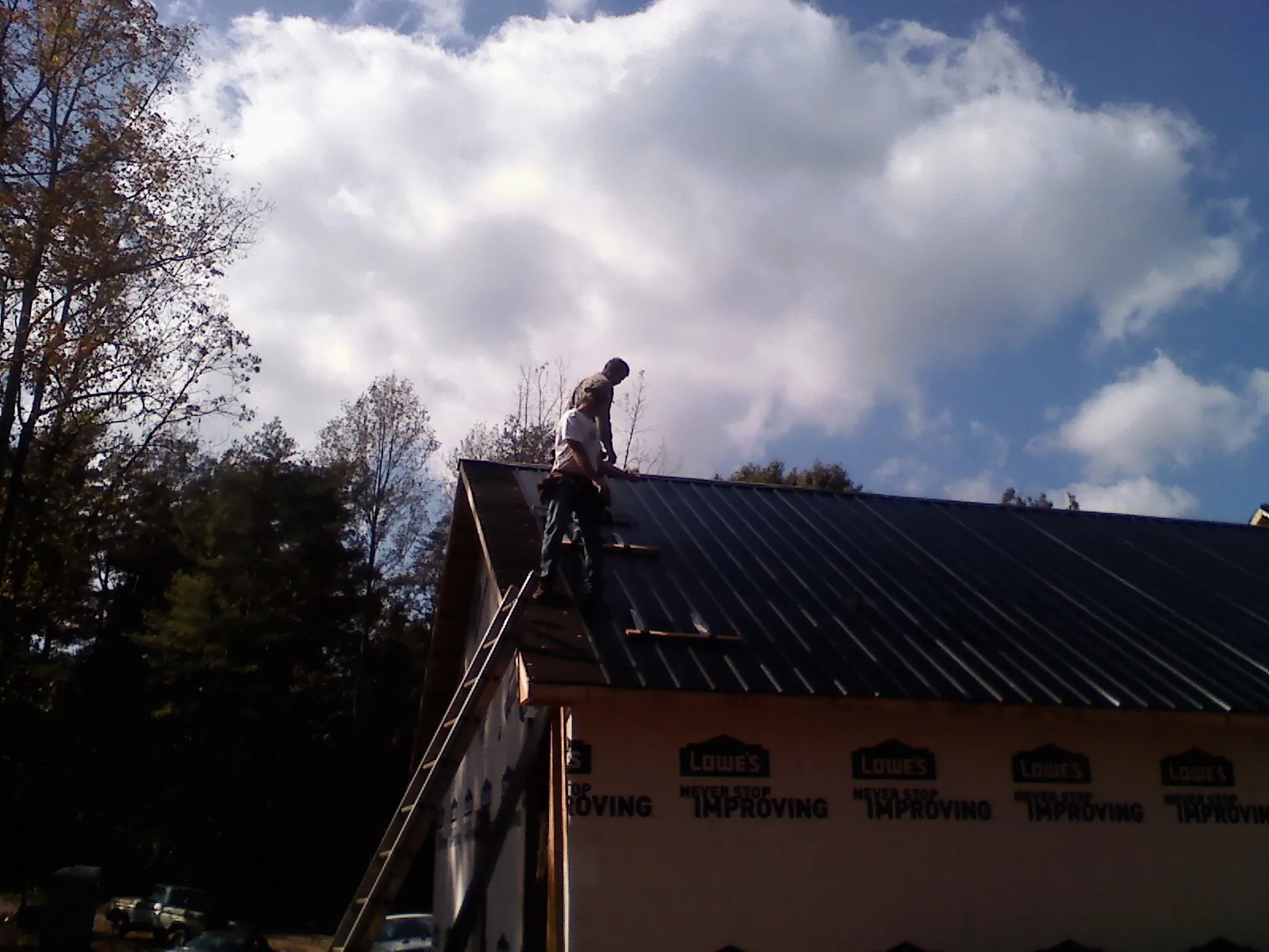 Roofer fastening dark metal panels high against a cloudy sky, from a Roof Inspection job in River Falls