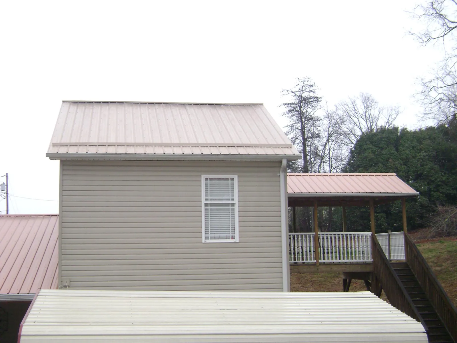 Tan metal roofs on a two story addition and attached porch, from a Roof Replacement job in River Falls